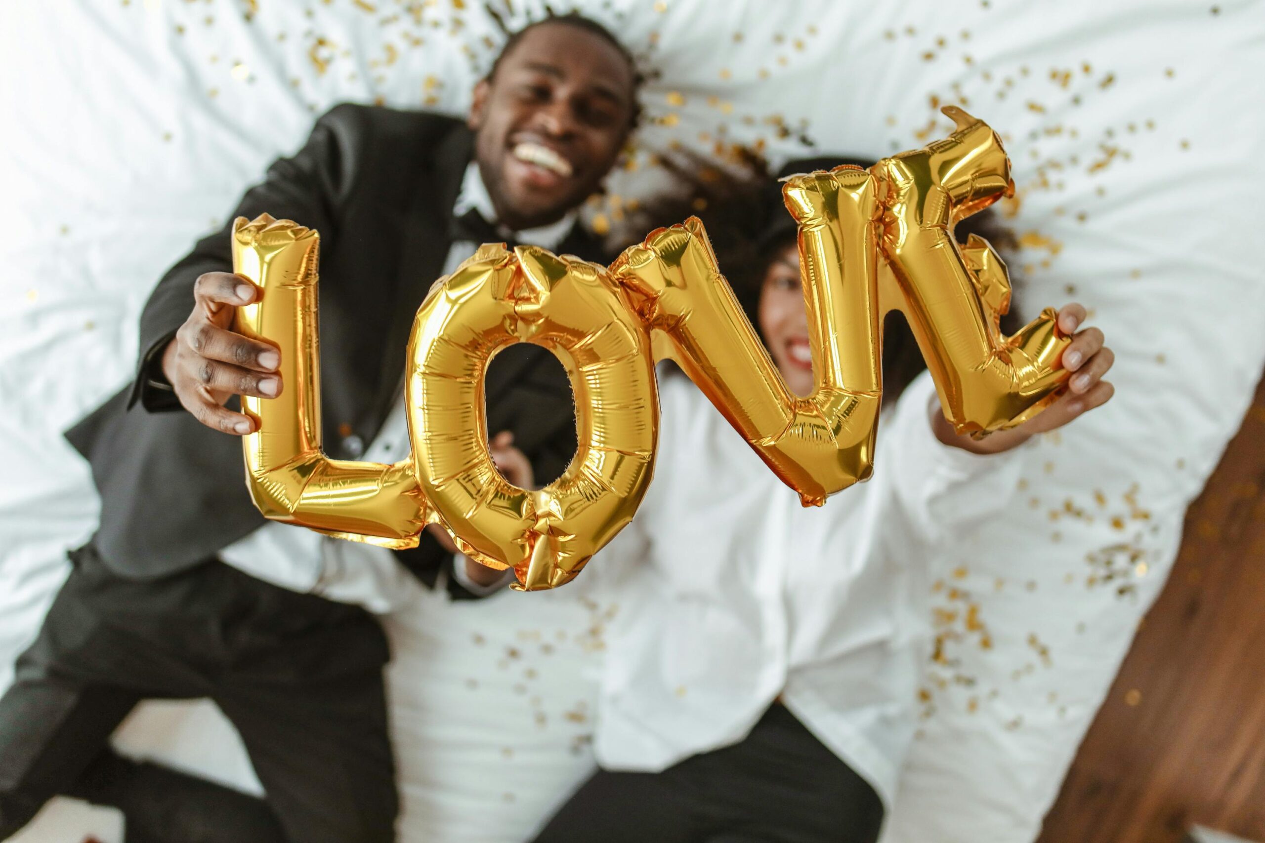 adorable couple lying down holding up a gold love balloon